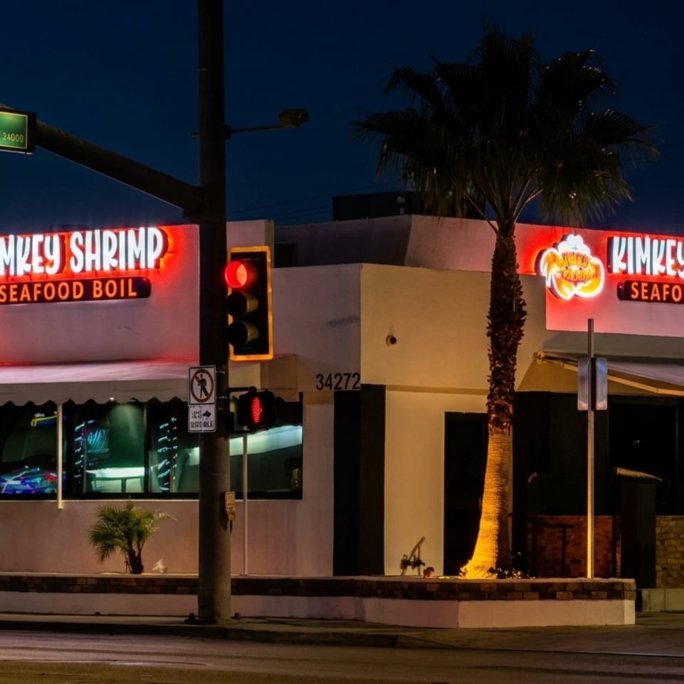 Exterior of Kimkey Shrimp Seafood Boil restaurant at night, with bright neon signs and a palm tree.